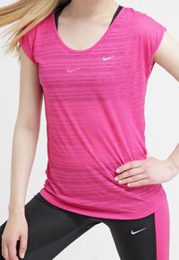 Rosa kortärmad träningströja med rundad halsringning och strukturerade ränder, med en liten vit Nike-logga på bröstet. I kombination med svarta leggings.