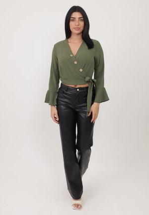 Top envolvente de color verde oliva con mangas acampanadas, con detalles de botones y un nudo lateral, combinado con pantalones de imitación cuero negro de talle alto.