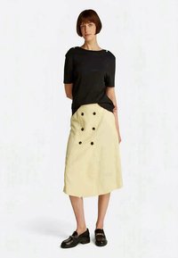 Black short-sleeve top, relaxed fit. Cream knee-length skirt with two rows of button accents, flat texture, and side pockets. Black loafers.