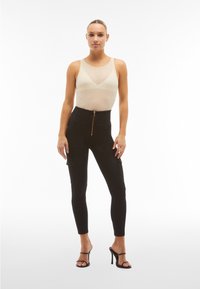 Pantaloni cargo neri a vita alta con zip anteriore, forma aderente e due tasche laterali. Abbinati a un top leggero e trasparente e tacchi con lacci.