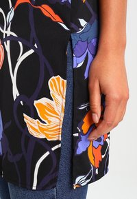 Bloemmotiefstof in het zwart met oranje, paarse en witte accenten. Heeft een zijsplit, een soepele textuur en een losse pasvorm.