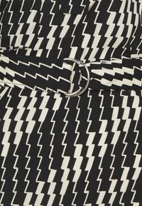 Tissu à motif zigzag noir et blanc avec une ceinture assortie dotée d'une boucle double anneaux argentée.