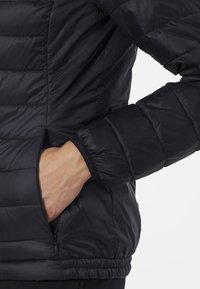 Giacca a vento nera con design trapuntato, dotata di polsini elastici e tasche laterali, realizzata in tessuto leggero e lucido.