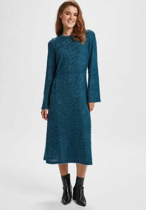 Teal, fuzzy knit dress with long sleeves and a round neckline. A-line silhouette falls mid-calf. Worn with black ankle boots.