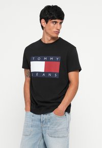 Must musta T-särk musta kangast, millel on ristkülikukujuline graafika, mis sisaldab punaseid, valgeid ja mereteemant siniseid plokke ning tekst "TOMMY JEANS", ümmargune kaelus, lühikesed varrukad.