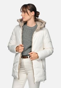 Giacca bianca imbottita con interno beige e cappuccio, dotata di chiusura lampo frontale, tasche laterali e tessuto strutturato. Indossata sopra un maglione grigio.