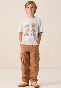 Lichtgrijs T-shirt met fietsenafbeeldingen in bruin, gecombineerd met tan cargobroeken met grote zijzakken en een relaxte pasvorm.