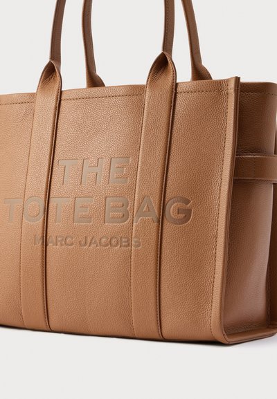 Geantă tote maro din piele texturată cu două mânere, având pe față textul în relief "THE TOTE BAG" și "MARC JACOBS".