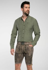 Grünes Langarmhemd mit Button-down-Kragen, kombiniert mit braunen Ledershorts mit dekorativen Nähten und einer passenden Schnalle.