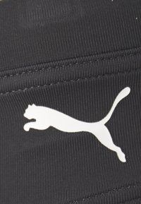 Schwarzer Stoff mit einer gerippten Textur, der ein auffälliges weißes Puma-Logo zeigt. Das Logo zeigt die Silhouette eines springenden Pumas.