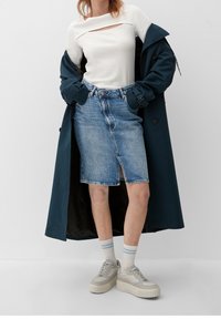 Valkoinen ribbiteksturilla varustettu pitkähihainen paita, jossa on aukko, farkkuhame, tumma trench-coat ja vaaleat sneakerit, joissa on paksu pohja. Sinivalkoiset raidalliset sukat.