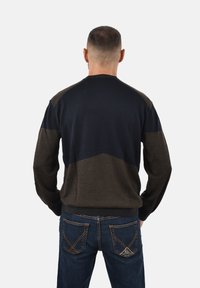 Maglione lavorato a maglia in blu scuro e marrone con un design geometrico sulle spalle. Abbinato a jeans in denim scuro con cuciture a contrasto.