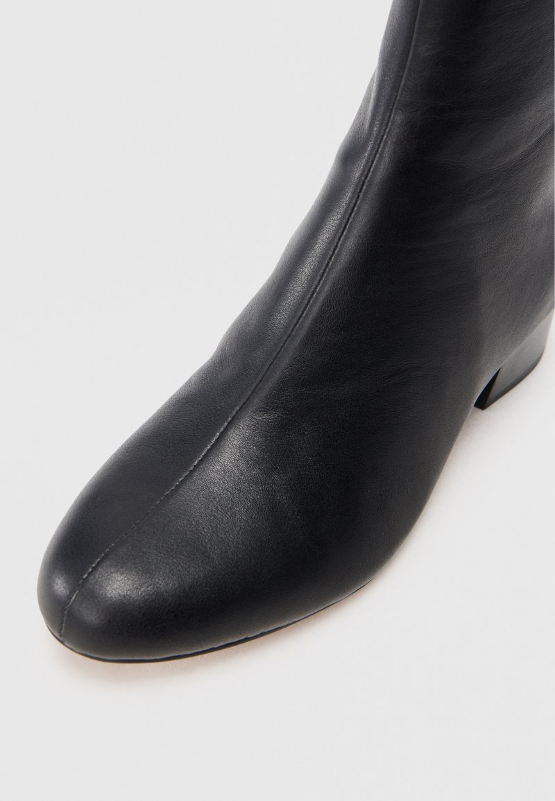 Stivale alla caviglia in pelle nera con una texture liscia, punta affusolata e dettagli di cucitura discreti. Include un tacco basso a blocco per maggiore stabilità.