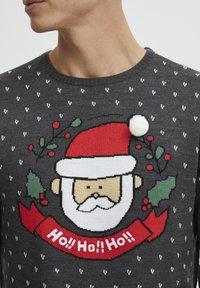 Pull en tricot gris avec un graphique de Père Noël portant un chapeau rouge, une barbe blanche et un pompon blanc. Comprend du houx décoratif et le texte "Ho!! Ho!! Ho!!".