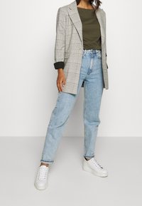 Blazer a quadri con accenti grigi e neri, top verde, jeans azzurri chiari e sneakers bianche. Presenta una vestibilità rilassata e maniche arrotolate.