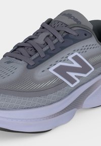 Γκρι αθλητικό παπούτσι New Balance με λευκή σόλα, επάνω μέρος από δίχτυ και γκρι κορδόνια, με μεγάλο λευκό και γκρι λογότυπο "N" στο πλάι.