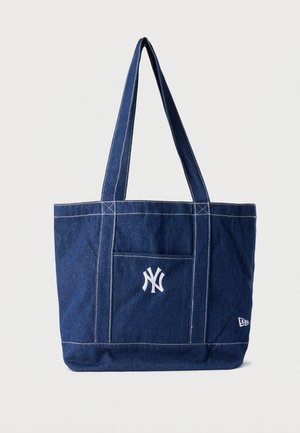 Bolsa tote de mezclilla azul con asas largas, costuras blancas cosidas, bolsillo frontal y logotipo blanco de los New York Yankees centrado en el bolsillo.