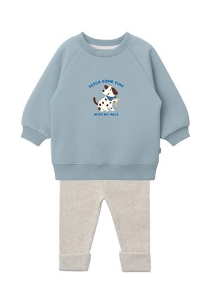 Hellblauer Pullover mit langen Ärmeln, versehen mit einem Hund und dem Text „Fetch some fun! With my pals“, kombiniert mit beigen, hochgekrempelten Hosen.