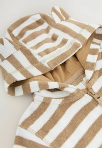 Serviette à capuche rayée en coton éponge beige et blanc. Présente de petites oreilles sur la capuche et une fermeture éclair à l'avant avec une doublure intérieure beige.