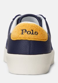 Navy leather sneaker with a white rubber sole. Features a textured yellow fabric heel tab with "Polo" embroidered in navy.