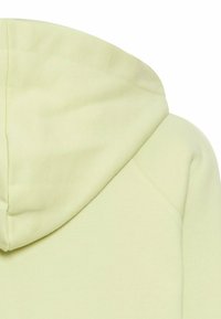 Jasnożółta bluza z kapturem, charakteryzująca się miękką fakturą, dużym kapturem i luźnym krojem. Widoczne detale przeszycia na ramionach i bokach.