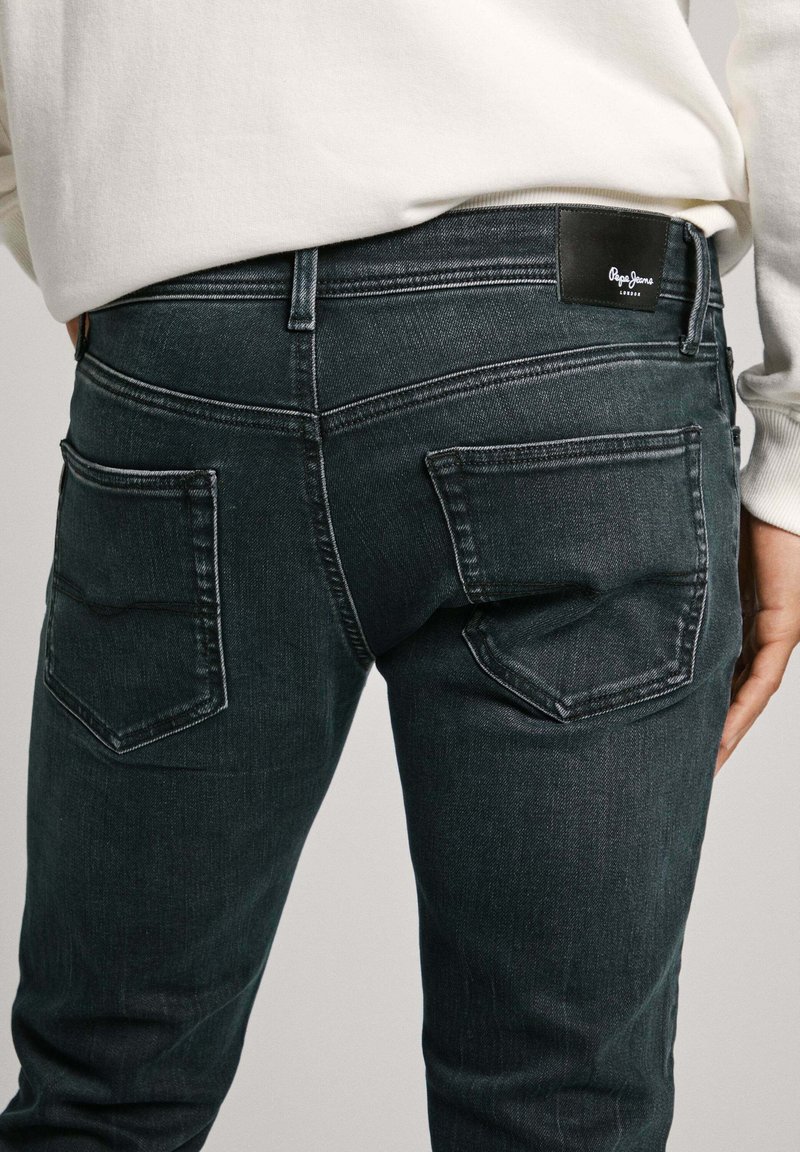 Dunkelblaue Jeans aus Denim mit einer taillierten Passform, vier Taschen und einem Lederlogo-Patch am Bund. Strukturierter Stoff mit sichtbaren Nähten.