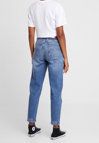 Ljusblå jeans med hög midja och avslappnad passform, fem fickor, blekt utseende och lätt slitage; kombinerat med en kortärmad vit t-shirt och svarta sneakers.