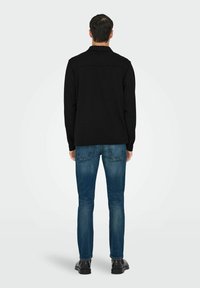 Must mustaga kaelusega jakk, mis on valmistatud pehmest kangast, koos kitsaste siniste teksadega. Komplektil on puhas, minimalistlik disain.