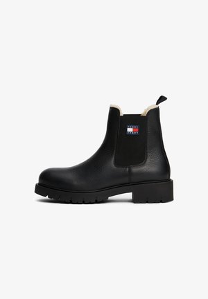 Black leather ankle boot with thick sole, elastic sides, shearling lining, and Tommy Jeans logo on the outer side.