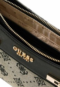 Portefeuille zippé noir et beige avec ferrures dorées, présentant un extérieur à motif et plusieurs compartiments intérieurs. Logo de la marque visible.
