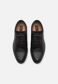 Chaussures en cuir noir avec une finition lisse, dotées de lacets ronds, d'accents perforés sur les côtés et d'une semelle intérieure rembourrée.