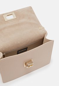 Beige Lederhandtasche mit strukturierter Oberfläche, goldfarbenen Beschlägen und einem Schlossverschluss. Das Innere verfügt über ein glattes Futter und ein Markenetikett.