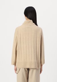 Bežs turtleneck džemperis izgatavots no struktūras adījuma auduma, ar vertikālu ribu, vaļīgu piegriezumu un plašām piedurknēm, apvienots ar vaļīgām bežām biksēm.
