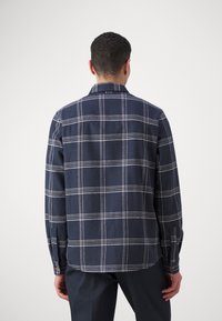 Camicia a quadri blu navy con linee bianche, con polsini abbottonati e yoke posteriore. Tessuto morbido e design di vestibilità regolare. Ha un orlo arrotondato nella parte inferiore.
