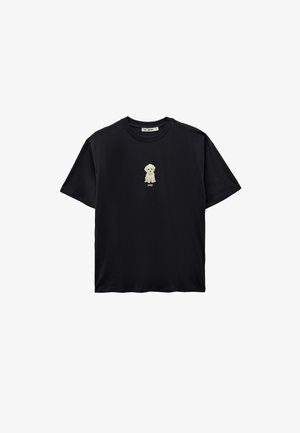 Musta lyhythihainen T-paita, jossa on keskellä rintaa pieni kirjailtu beige pentu ja sen alapuolella sana "puppy".