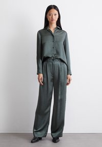 Blouse en satin vert avec col et fermeture à boutons, associée à un pantalon ample assorti. Texture lisse et drapé élégant.
