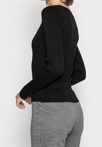 Svart ribbad tröja med långa ärmar och en åtsittande design, matchad med svart och vit rutiga byxor. Slät textur, klassisk stil.