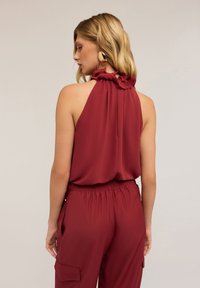 Top senza maniche bordeaux con scollo arricciato e vestibilità rilassata, abbinato a pantaloni cargo coordinati con tasche laterali e vita elastica.