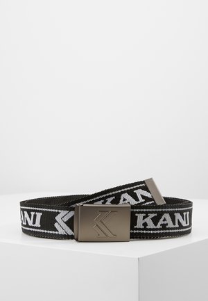 Ceinture en tissu noire avec texte blanc "KANI" et boucle en métal embossée d'un logo "K" stylisé, présentée sur une surface blanche.