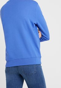 Niebieski bawełniany sweter z długimi rękawami i ściągaczem u dołu, w połączeniu z ciemnymi dżinsami o klasycznym fasonie tylnej kieszeni.