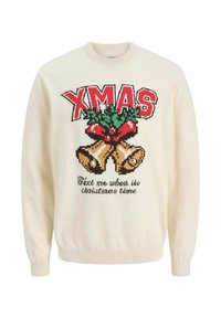 Maglione color crema con una grafica festiva di campanelle e agrifoglio, con testo rosso "XMAS" e la scritta "Mandami un messaggio quando è Natale" in nero.