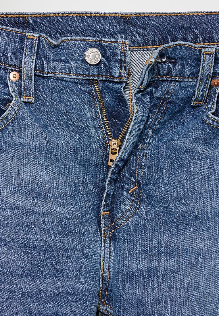 Denim-Jeans in Mittelblau, mit einem Reißverschluss, kupferfarbenen Nieten und orangefarbener Naht. Klassisches Fünf-Taschen-Design mit weicher Textur.