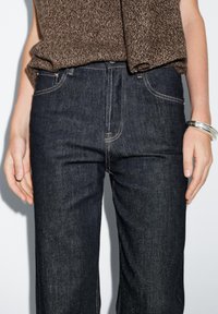 Jeans in denim scuro con taglio a gamba dritta, cuciture a contrasto, design a cinque tasche e vita media. Maglione strutturato visibile sopra.