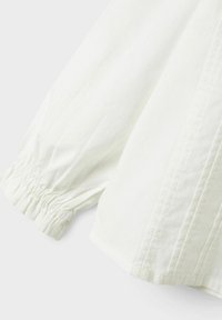 Witte lange mouwen met elastische ruche bij de manchetten en zichtbare stikdetails op lichte stof.