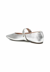 Zapato plano plateado con punta afilada, superficie texturizada y una correa al tobillo con ojales decorativos de metal. Suela plana, diseño casual.