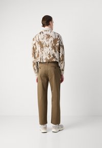 Brown and white patterned sweater, almond-colored chinos, and light sneakers. The sweater features a ribbed collar and loose fit.