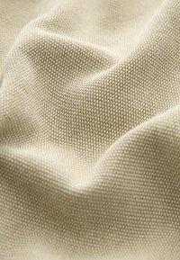 Beige kudottu kangas, jossa on teksturoitu pinta, esittelee tiheän ja tasaisen kudonnan sekä hienovaraisia vaaleuden vaihteluita pinnalla.