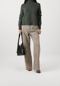 Zielony wełniany sweter z golfem, luźne beżowe spodnie z denimu oraz czarna skórzana torebka. Charakteryzuje się szerokimi nogawkami i paskami na torebce.