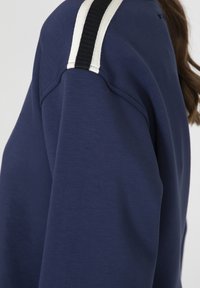 Felpa blu navy con tessuto testurizzato, presenta strisce verticali in bianco e nero sulle spalle e una vestibilità comoda.