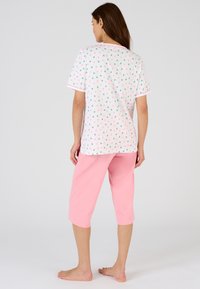 Conjunto de pijama de algodón que incluye una blusa blanca de manga corta con patrones de frutas multicolores y pantalones cortos rosas. Textura suave, ajuste relajado.